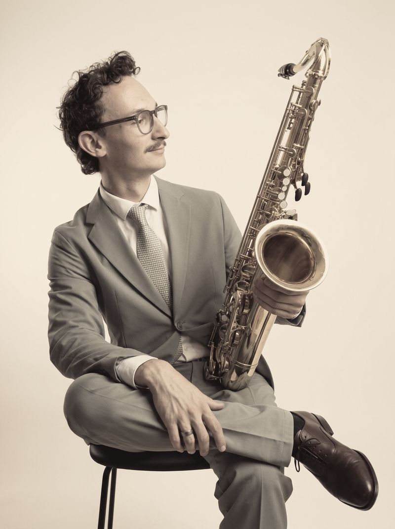 Porträt von Johannes im hellen Anzug, mit Tenorsaxophon auf einem Barhocker